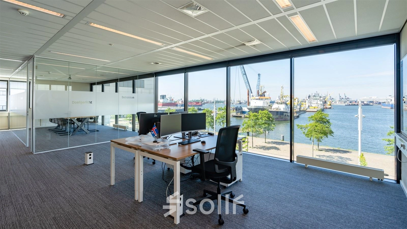 Bright office space with large windows overlooking Rotterdam Waalhaven, featuring desks and chairs for rental. Ideal workspace with modern amenities for business professionals.