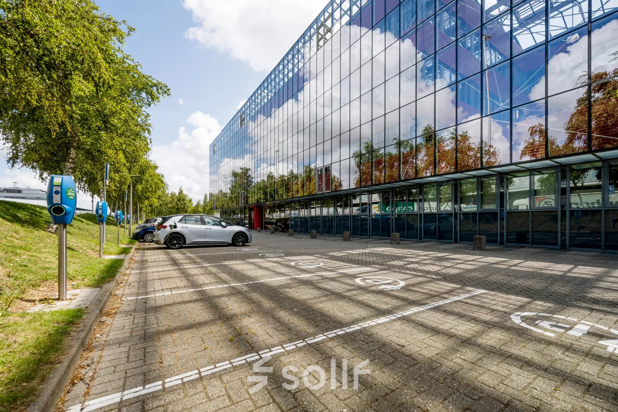 Exterior view of an office building at Folkstoneweg 2-56, Schiphol Airport, featuring reflective glass windows and adjacent parking spaces, highlighting opportunities for office space rental.