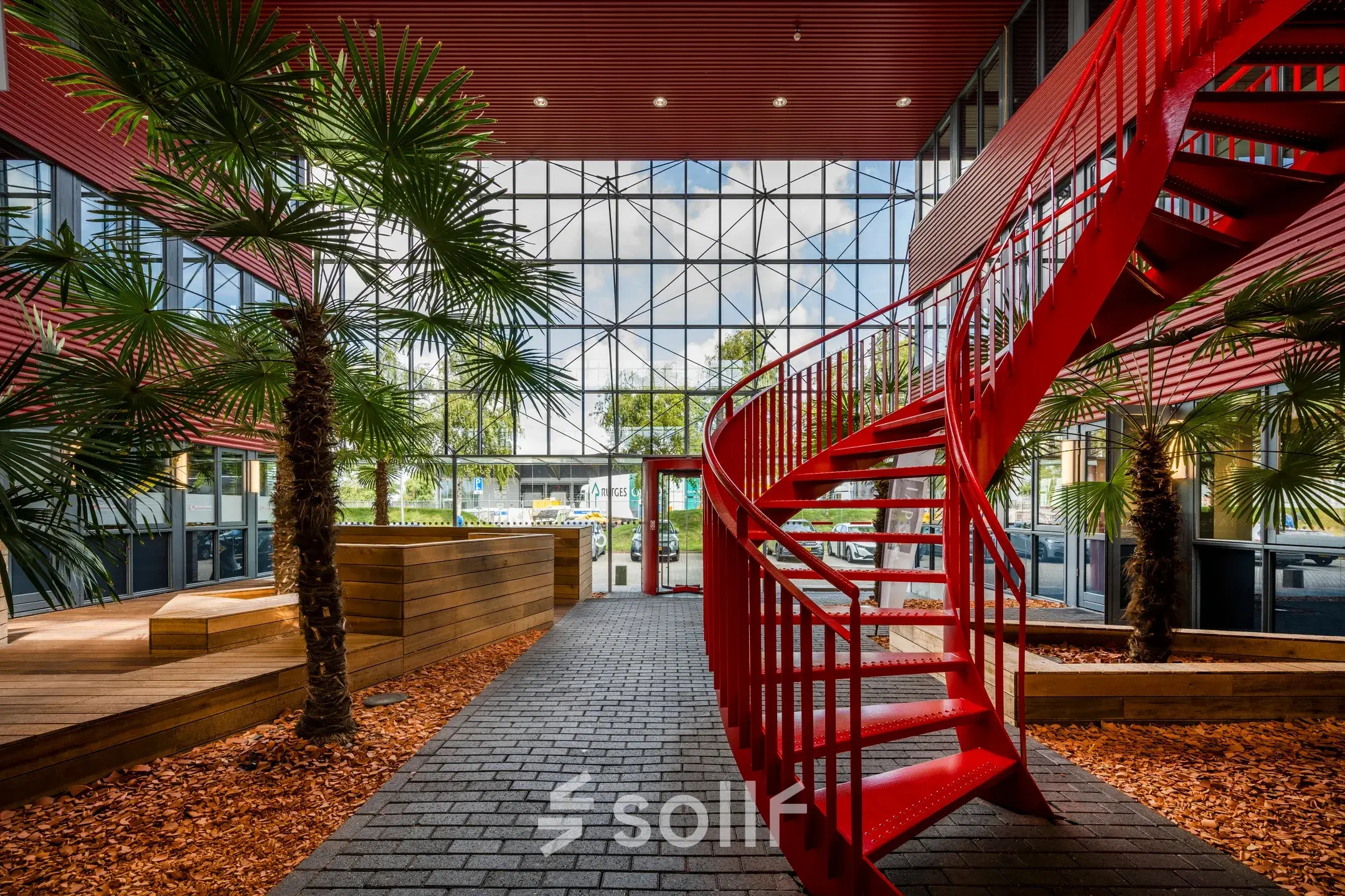 Bright office space in Schiphol Airport with a striking red spiral staircase and indoor greenery.