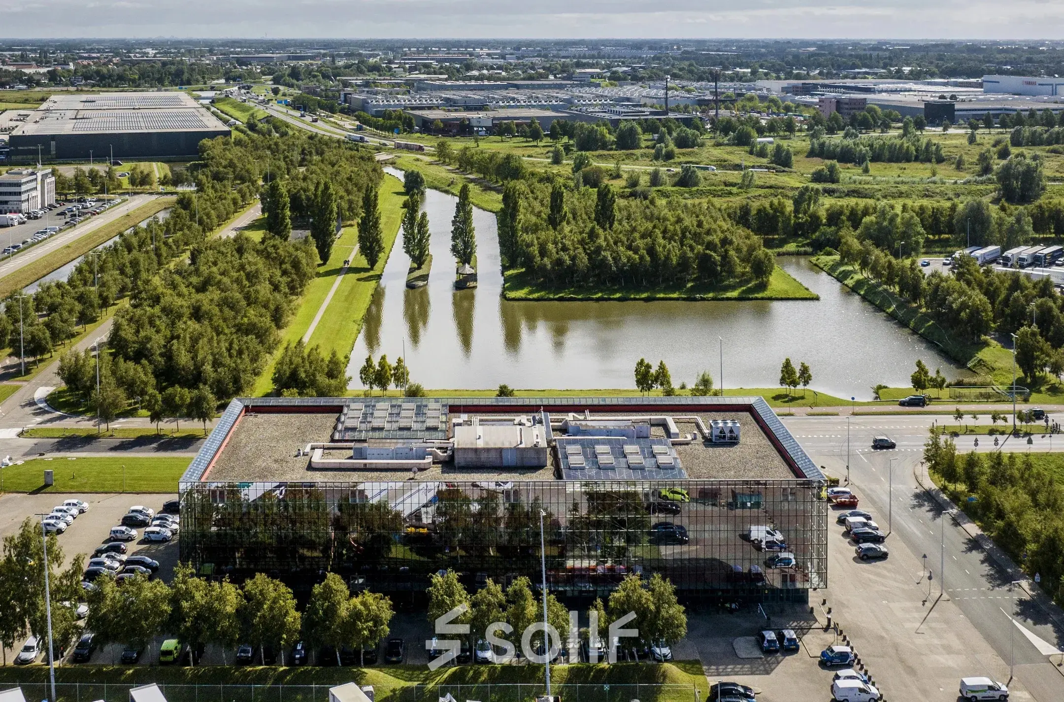 Aerial view of a modern office building surrounded by greenery and water at Schiphol Airport.