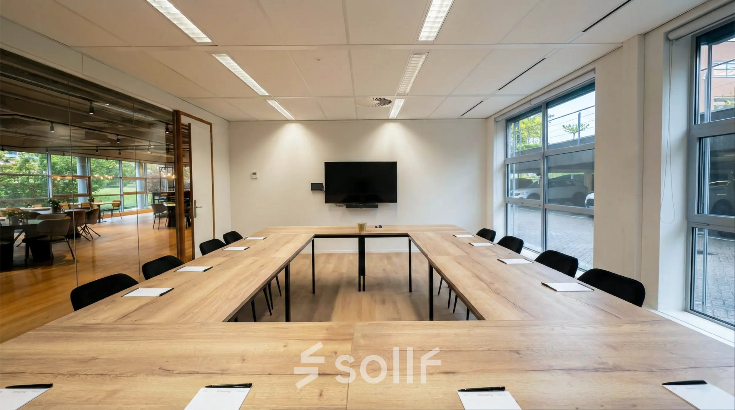 A bright conference room at Boeing Avenue 1-19, Schiphol Rijk, featuring a U-shaped wooden table, chairs, and a wall-mounted screen, ideal for office space rental.