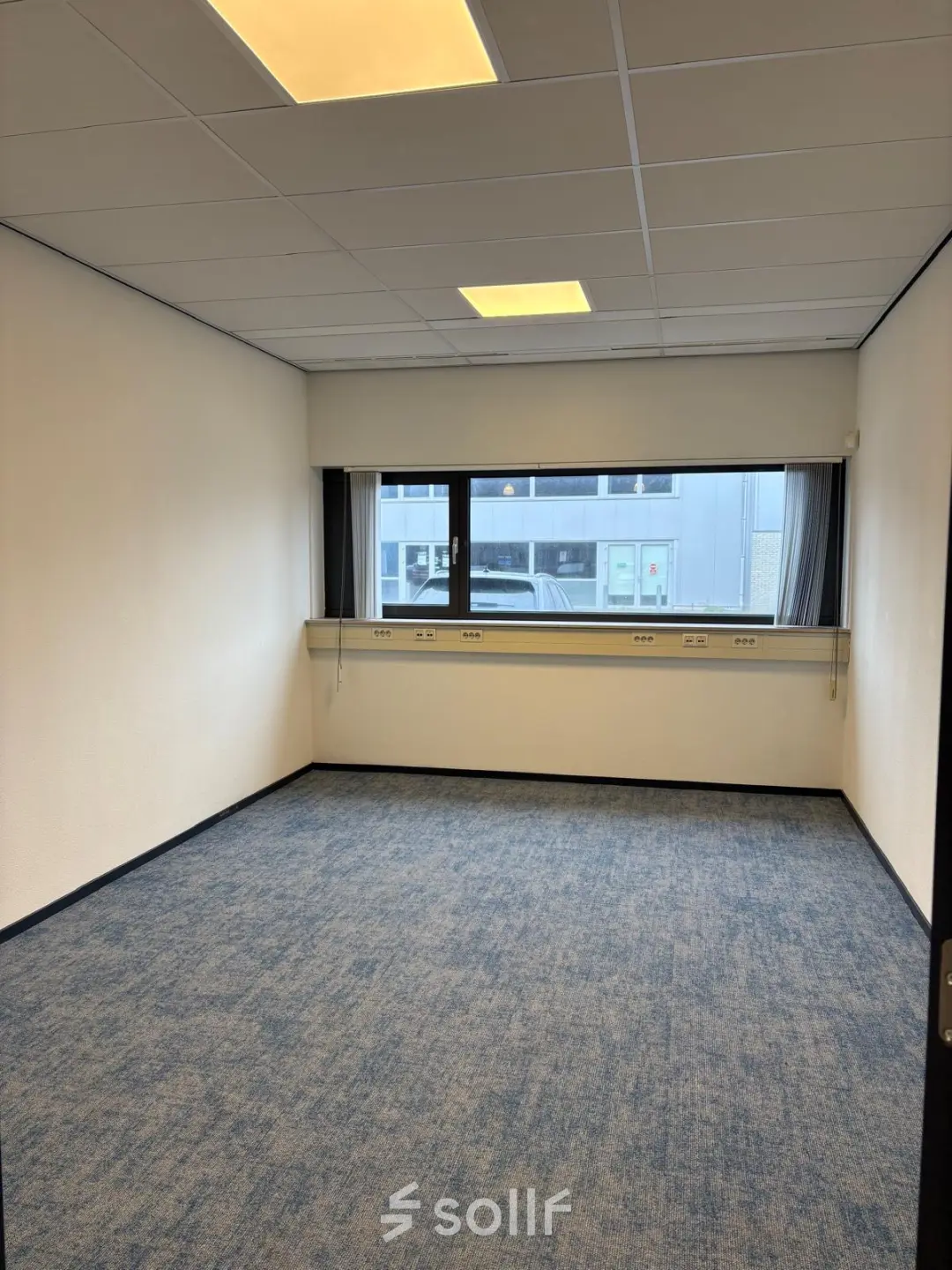 Unfurnished office space at Fischerpad 106 in Sittard available for rent, featuring blue carpet and wide windows.