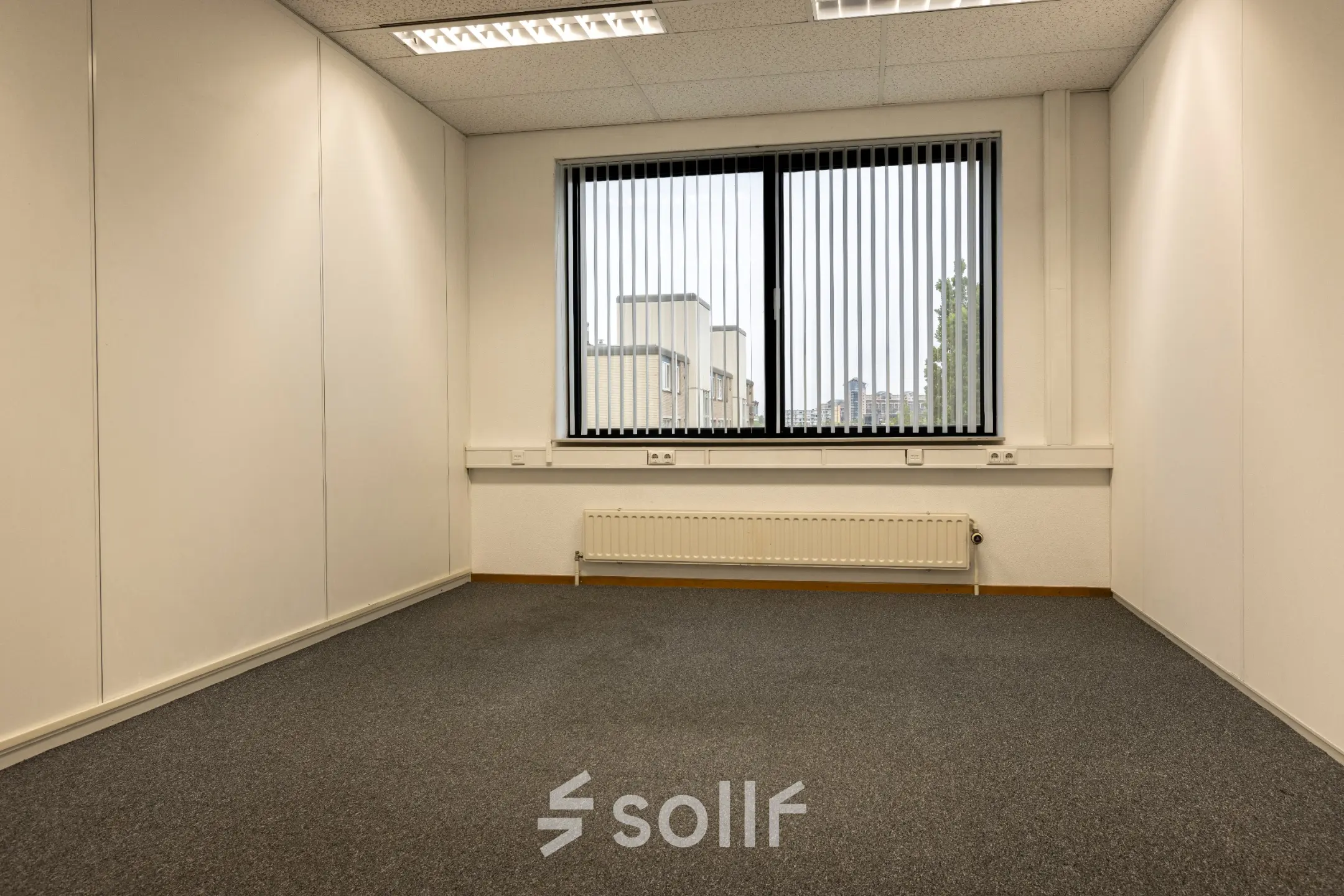 Empty office space at Curieweg 9, Spijkenisse, available for rent. The room features a window with vertical blinds and overhead fluorescent lighting.
