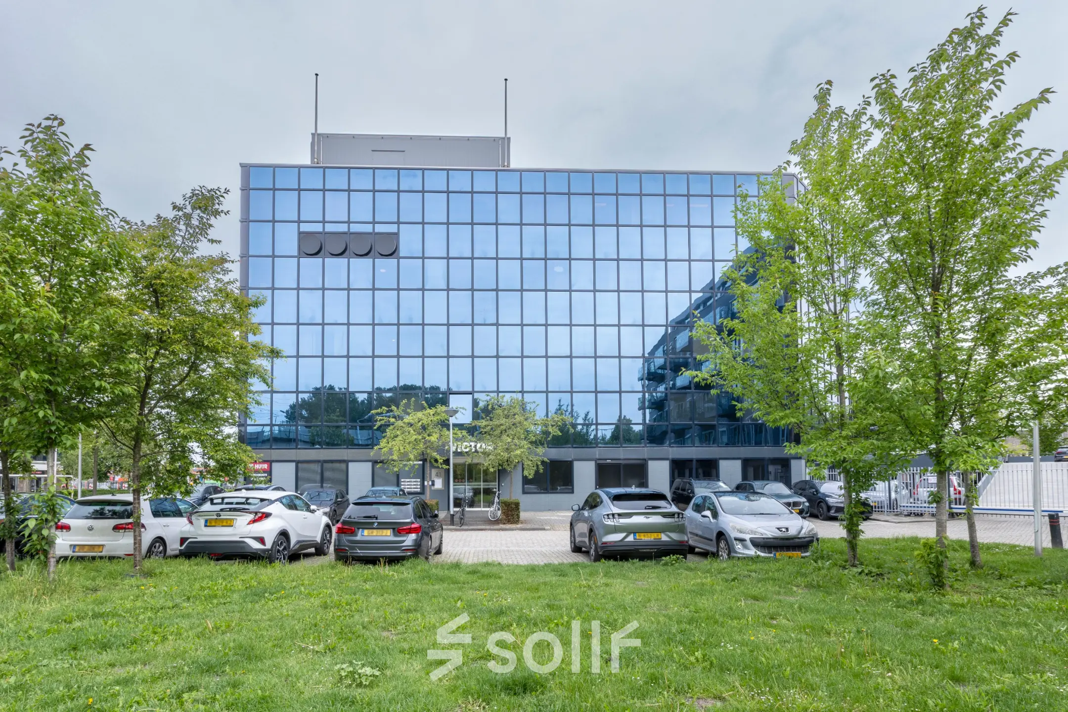 Exterior view of office space rental at Curieweg 9, Spijkenisse with a modern glass facade and parked cars in front.