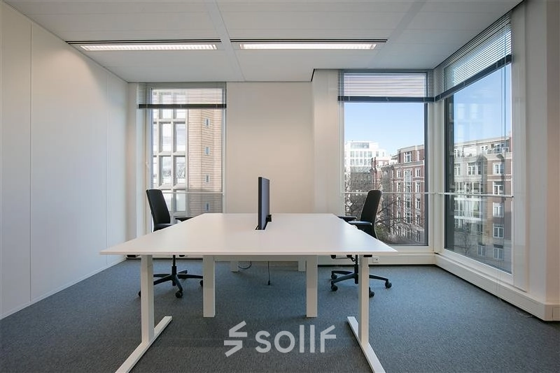 Modern office space rental at Alexanderveld 5-9, The Hague Center, featuring a bright workspace with large windows, two desks, and chairs, ideal for professional collaboration.