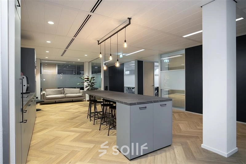 Modern office interior at Alexanderveld 5-9, The Hague, featuring a stylish open floor plan with a central table, sleek lighting, and ample seating, ideal for office space rental.
