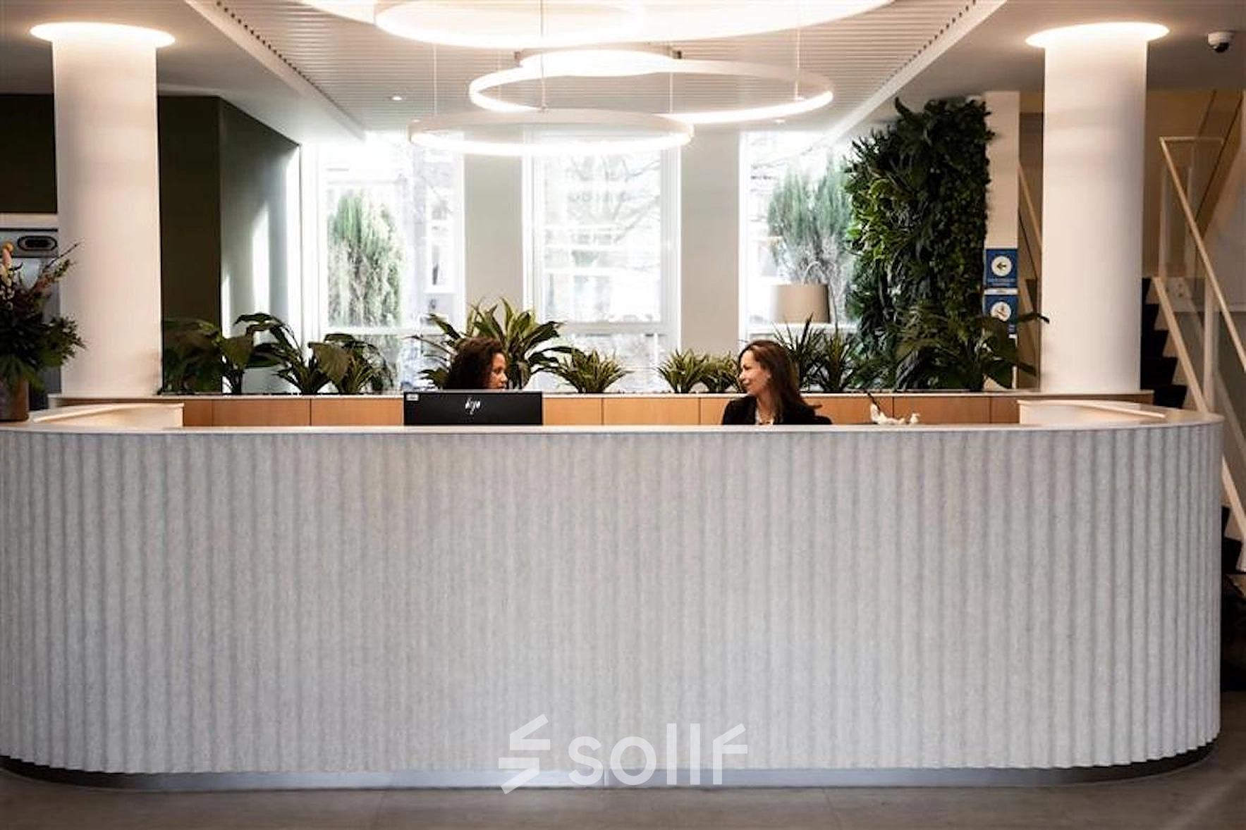 Modern, inviting reception area at Alexanderveld 5-9, The Hague Center, featuring a curved front desk and greenery, ideal for office space rental.
