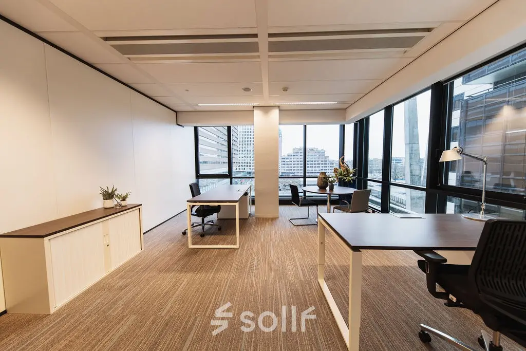 Modern furnished office space to rent at Anna van Buerenplein 41, The Hague Center, featuring well-lit workstations with large windows offering city views.