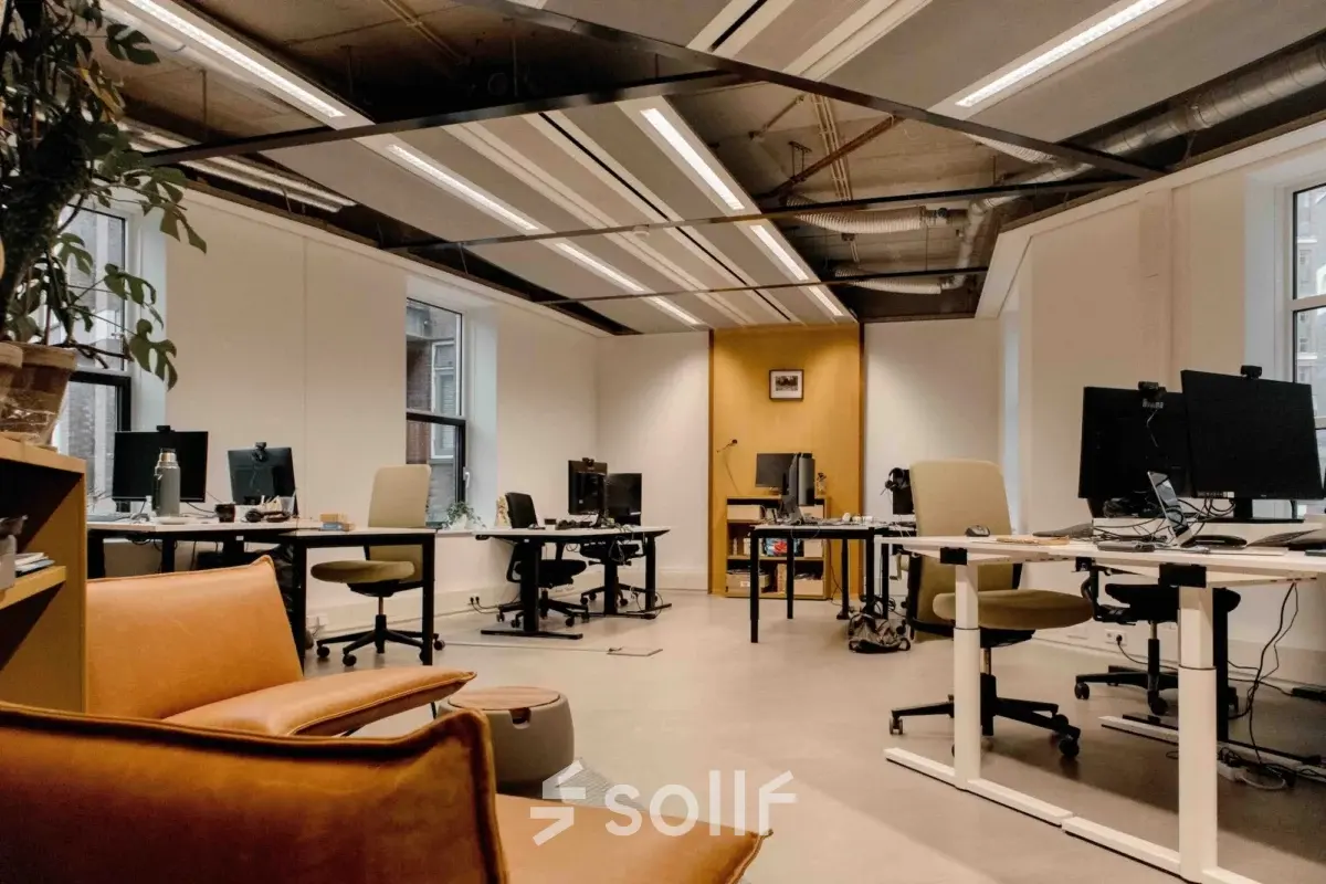Spacious office with several desks and chairs, featuring modern lighting and a relaxed seating area, ideal for anyone looking to rent office space in The Hague Center.
