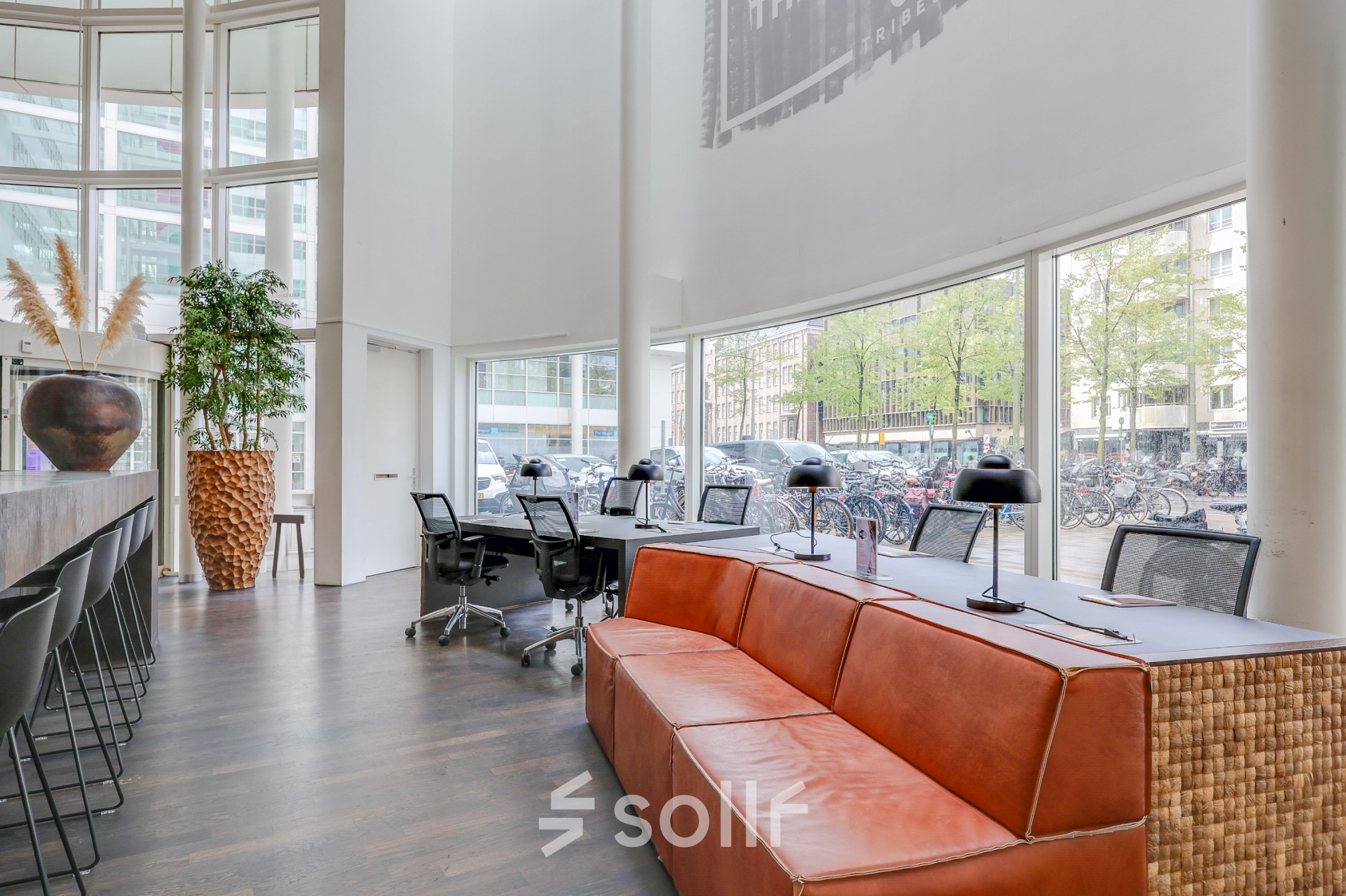 Stylish office available for rent at Kalvermarkt 53 in The Hague Center, featuring floor-to-ceiling windows, ergonomic chairs, and shared workspaces with modern furnishings.