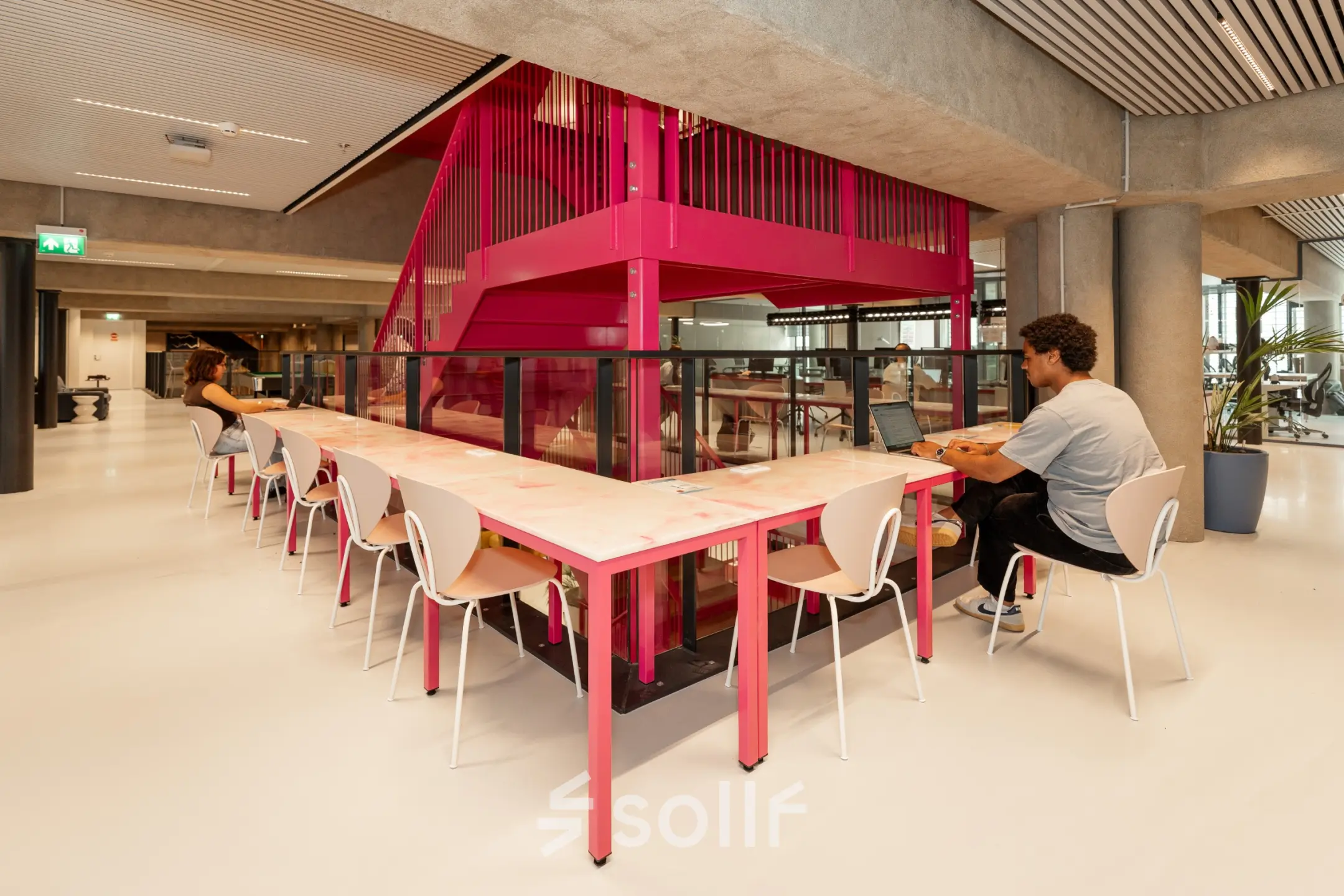 Modern office space rental at Waldopstraat 5, The Hague Center, with people working at communal desks near a vibrant staircase.