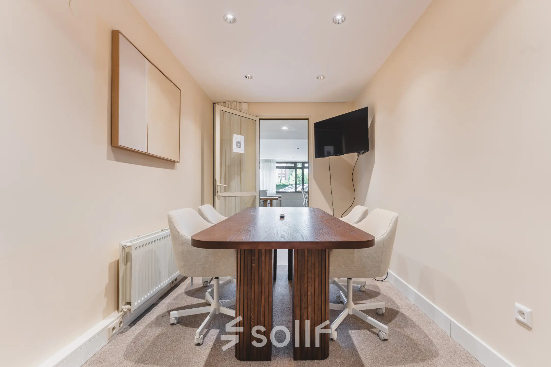 Cozy furnished office space for rent at Zeestraat 100 in The Hague Center, featuring a wooden table, chairs, wall-mounted TV, and natural lighting.