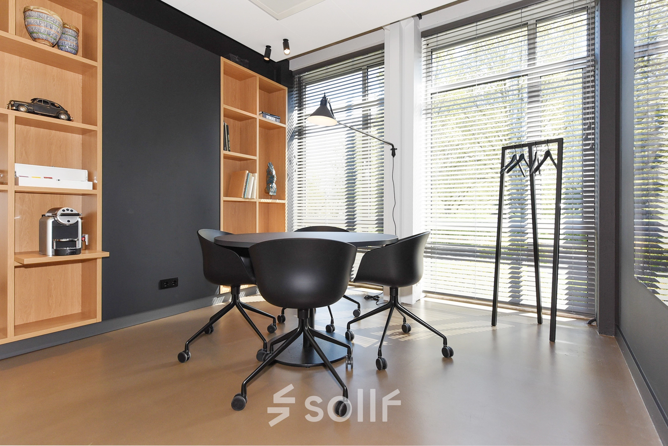 Furnished office space with a small round table and chairs, bookshelf, coat rack, and a window with blinds for rent at President Kennedylaan 19, The Hague Statenkwartier.