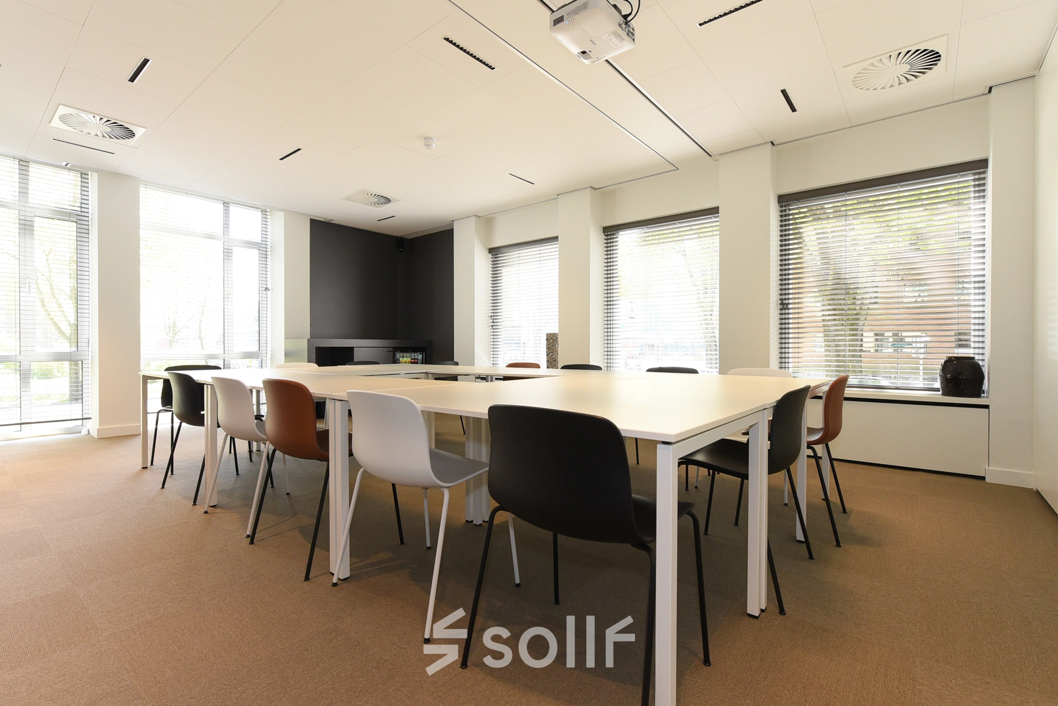 Bright office space rental in The Hague's Statenkwartier at President Kennedylaan 19, featuring a large meeting table and modern furnishings with natural light streaming through wide windows.