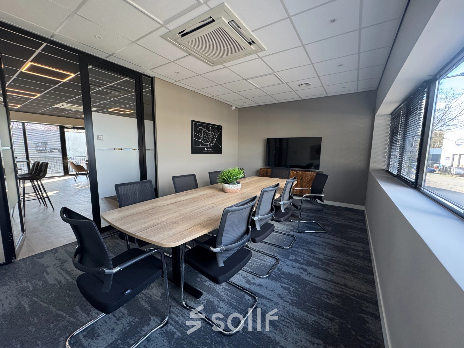 Bright and modern conference room available for office space rental in Tilburg, featuring a large wooden table, comfortable chairs, and a flat-screen TV.