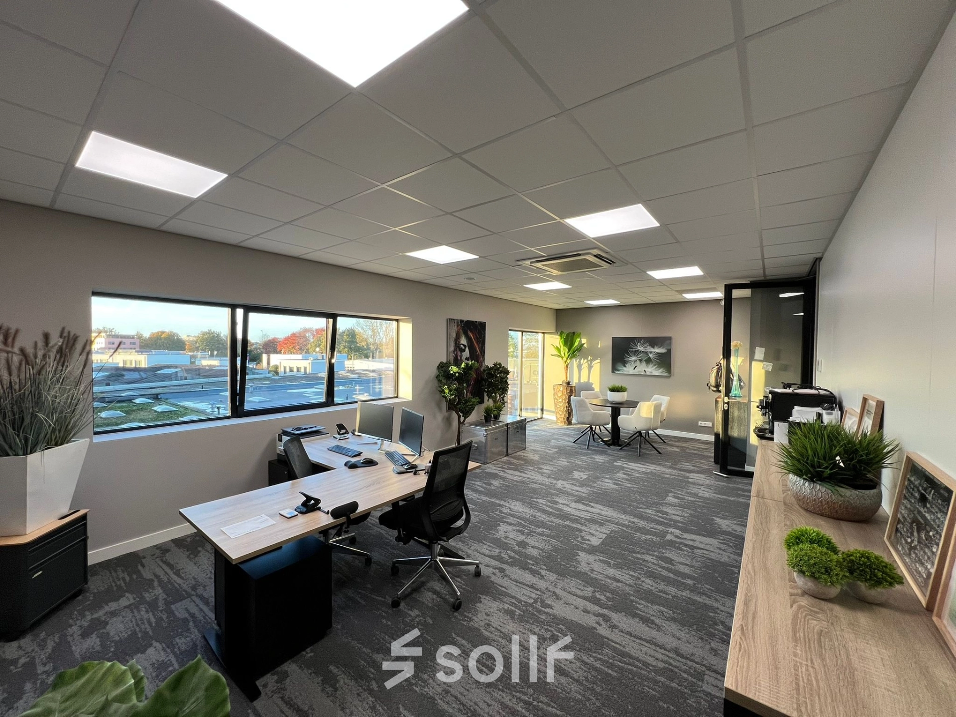 Bright, modern office space with large windows, sleek desks, and greenery, suitable for rent at Kapitein Rondairestraat 8, Tilburg. Ideal for those seeking office space rental.
