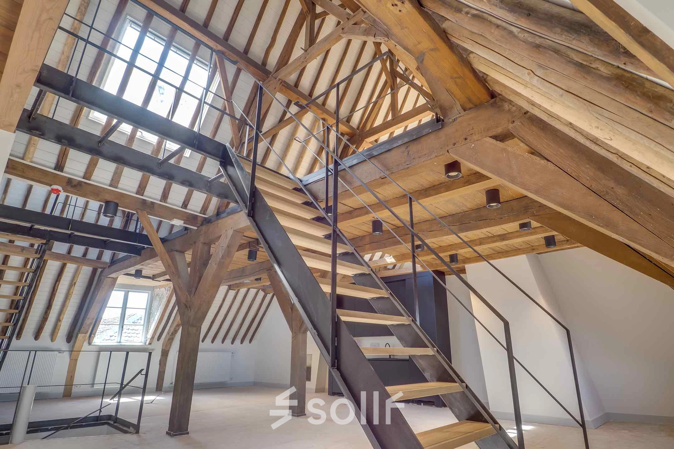 Spacious loft office space featuring exposed wooden beams, skylights, and a modern staircase at Brigittenstraat 22, ideal for rent office space in Utrecht Center.