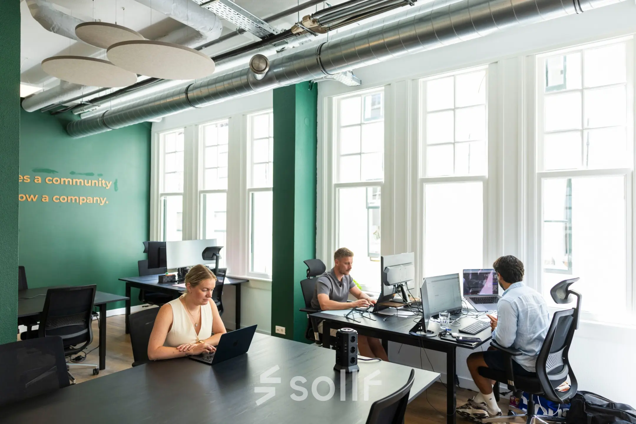 Modern office space rental at Oudegracht 161 in Utrecht Center with individuals actively working at desks near large windows.