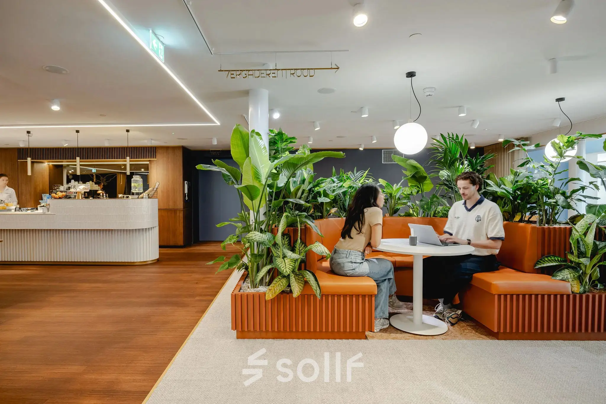 Modern office space at Moreelsepark 1, Utrecht Central Station with two people collaborating at a round table surrounded by plants, ideal for office space rental.