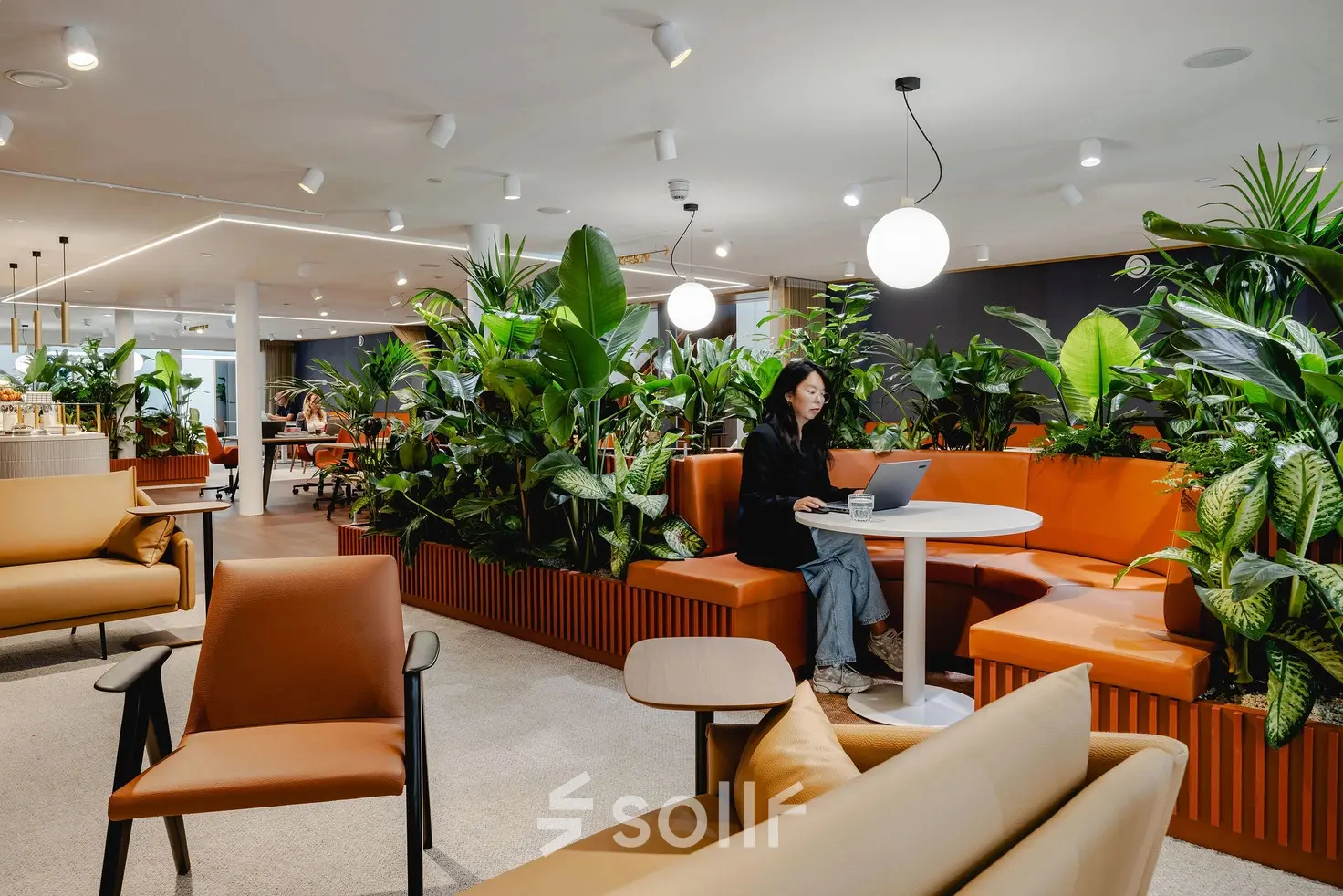 A modern office space rental at Moreelsepark 1, Utrecht Central Station, featuring stylish seating and greenery, with a person working on a laptop.