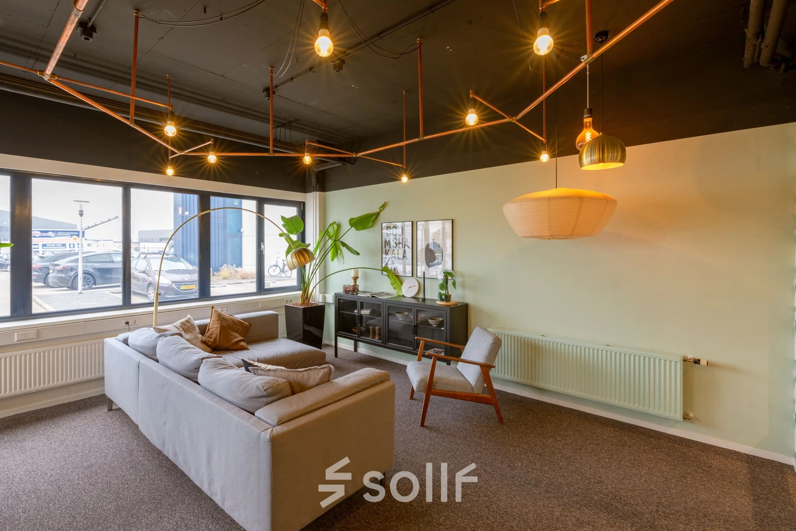 A well-lit office lounge area with modern lighting, a gray sofa, armchair, and decor. Ideal for office space rental at Atoomweg 400, Utrecht Lage Weide.