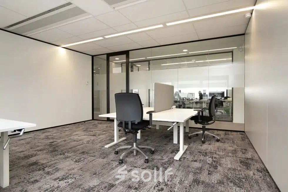 Modern office space featuring two desks with chairs, ideal for office space rental at Atoomweg 63, Utrecht Lage Weide. Large glass wall provides natural light and views of adjoining work areas.