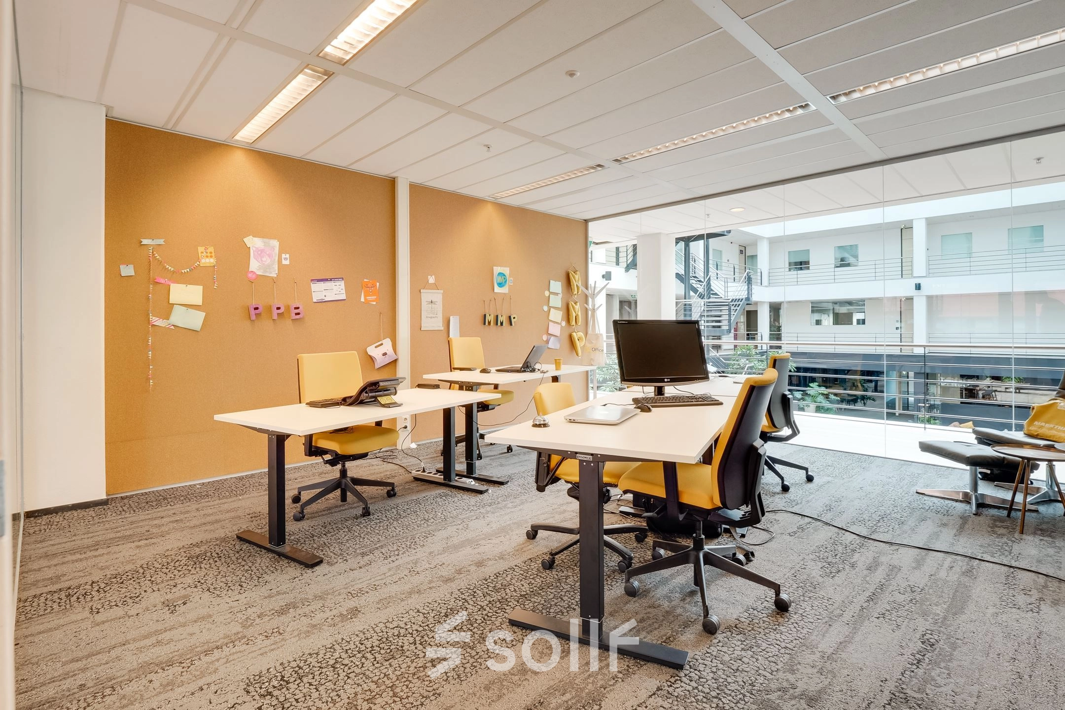 Bright office space with desks, chairs, and computers, suitable for office space rental at Computerweg 22, Utrecht Lage Weide, featuring a view of the indoor atrium.