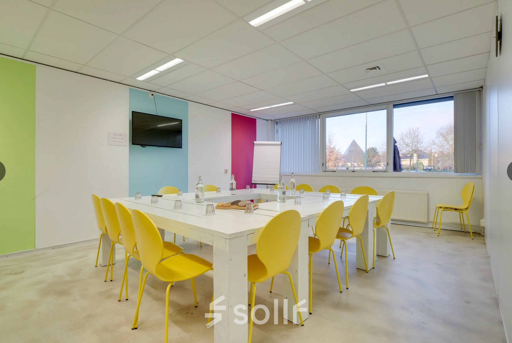 Bright office space for rent at Zonnebaan 18, Utrecht Lage Weide, featuring a meeting table with yellow chairs and natural light from a large window.