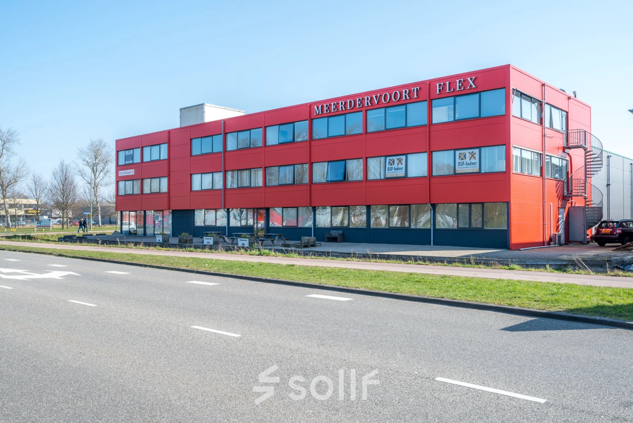 Exterior view of the office building located at Zonnebaan 18, Utrecht Lage Weide. The red facade stands out against a clear blue sky, perfect for office space rental.