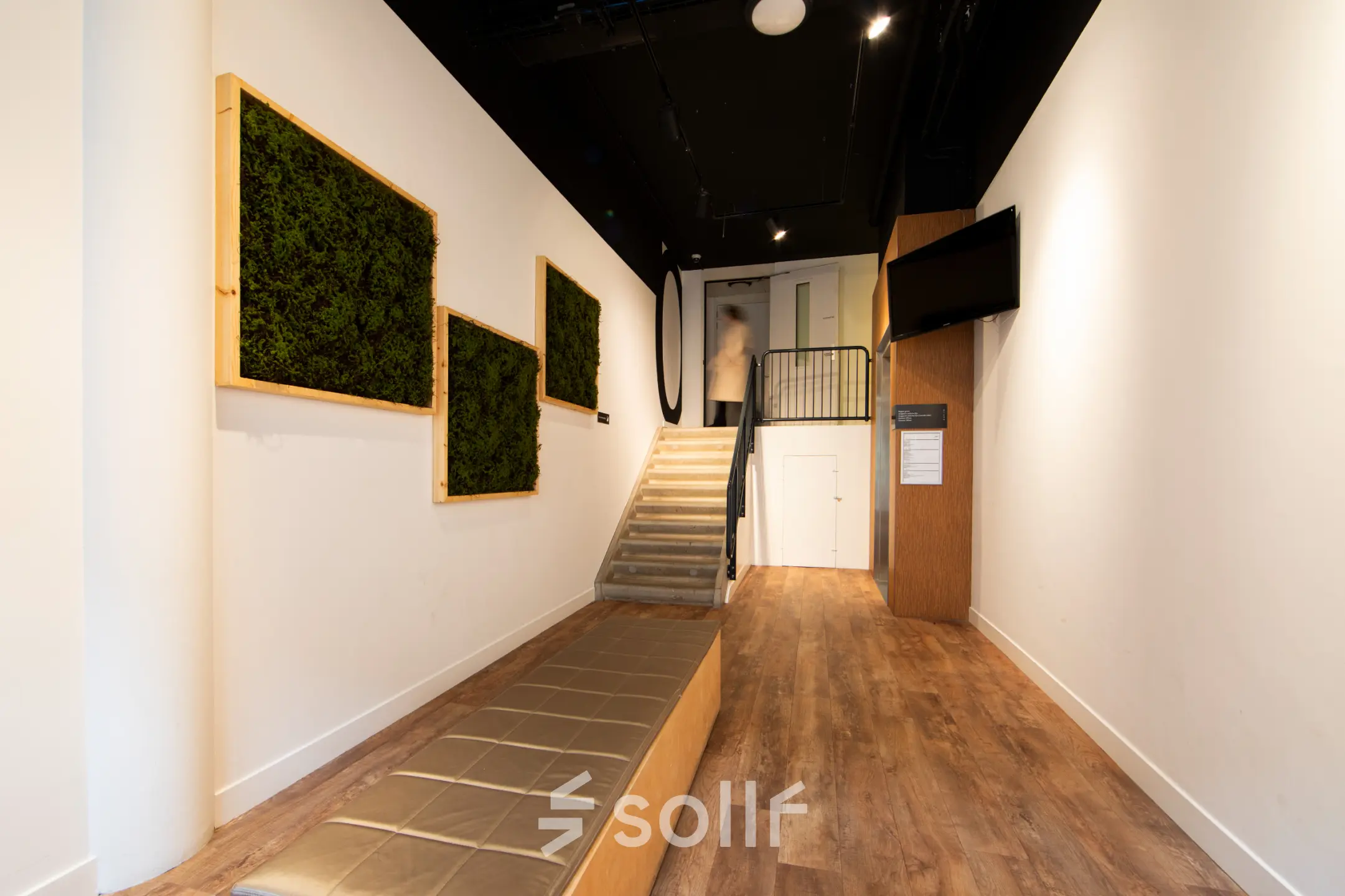 Modern office interior at Middenburcht 136 in Utrecht Leidsche Rijn, featuring wooden flooring, decorative wall art, and a staircase with a person ascending. Ideal for office space rental with easy access.