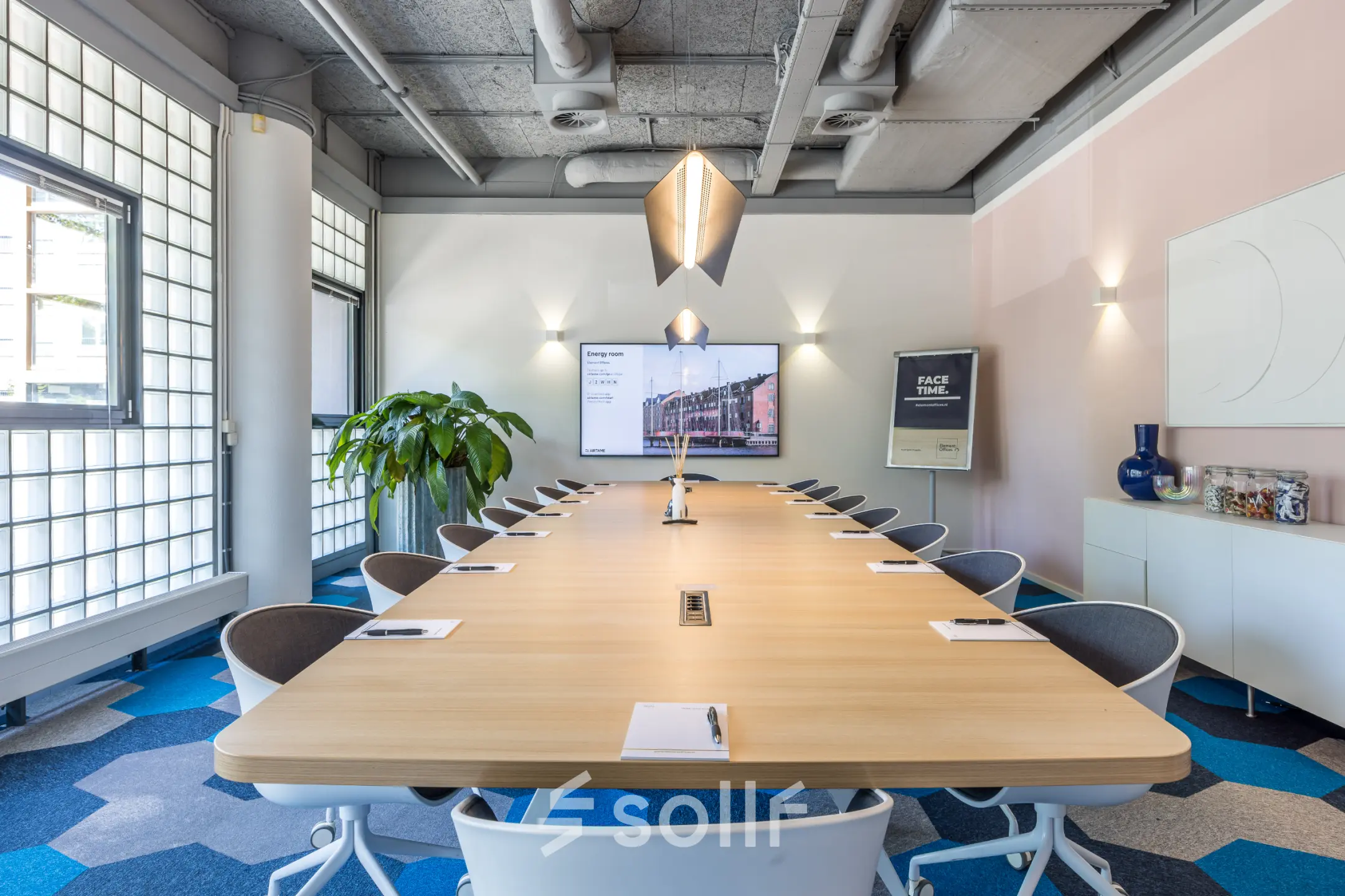 Bright conference room with a long wooden table, blue geometric carpet, and a large screen at Goeman Borgesiuslaan 77, perfect for office space rental in Utrecht North.