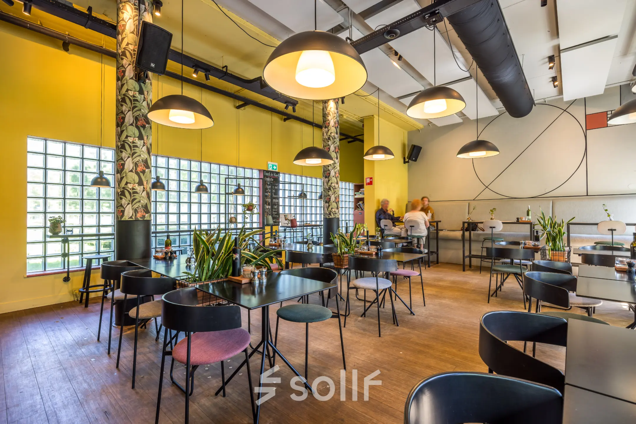 Furnished office space at Goeman Borgesiuslaan 77 in Utrecht North with tables and chairs, plants, and people in conversation. Ideal for office space rental.