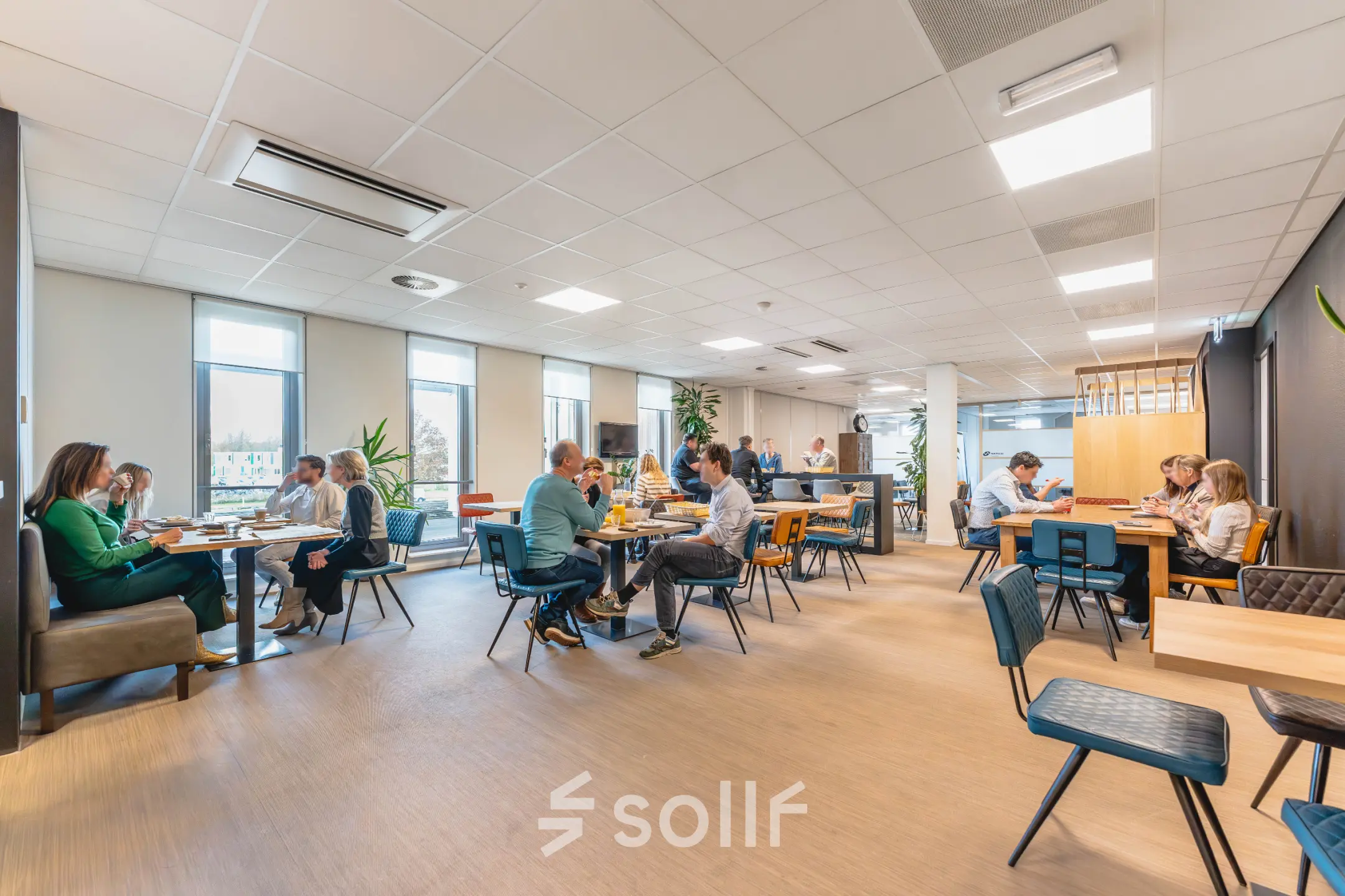 A bright and bustling office space at Orteliuslaan 850, Utrecht Papendorp, with groups of people engaged in discussions at tables. Ideal for office space rental.