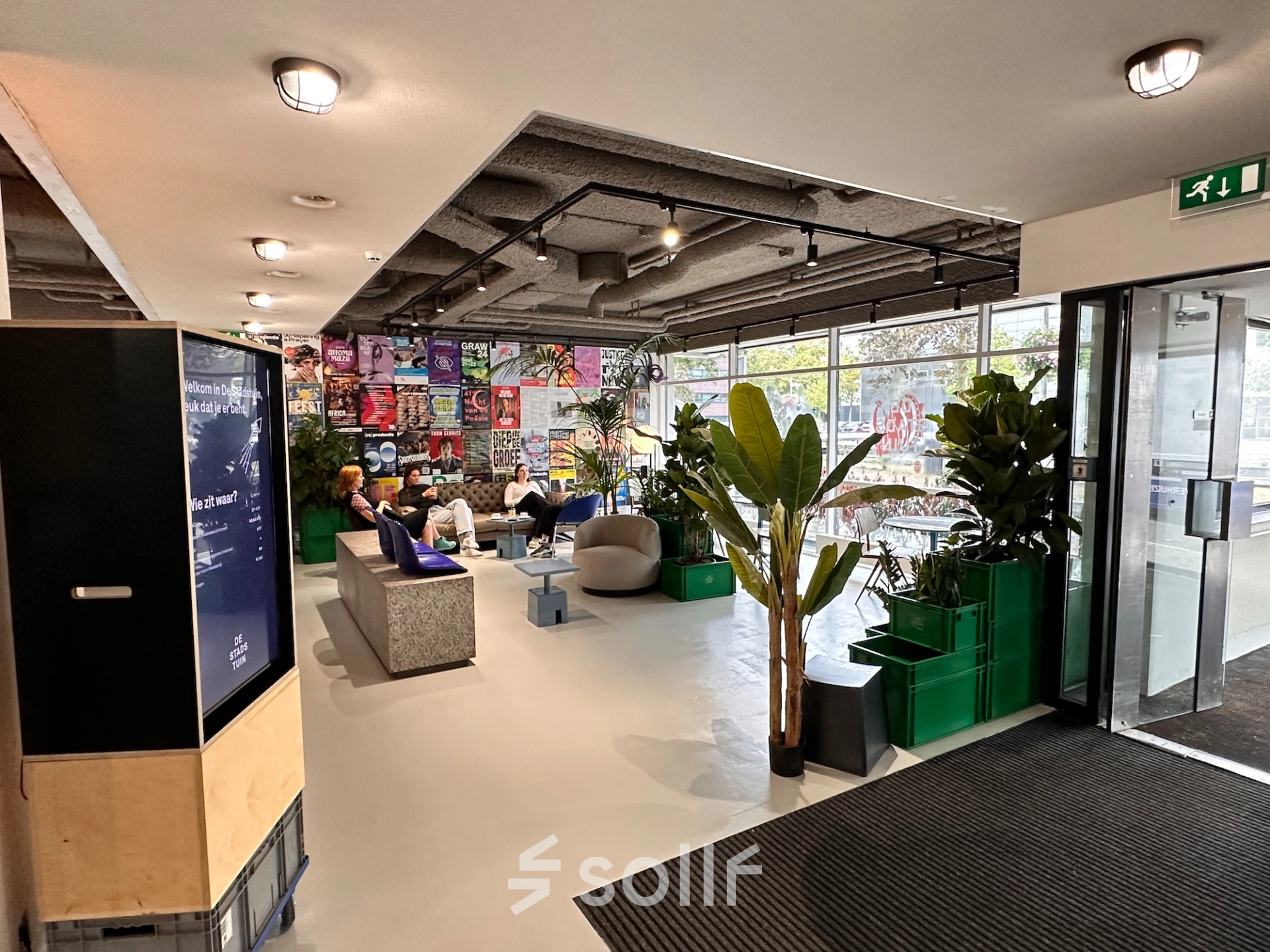 Spacious and creatively designed office lounge at Daltonlaan 200, Utrecht Rijnsweerd with modern furnishings and large windows, ideal for office space rental. People are engaged in casual business discussions.
