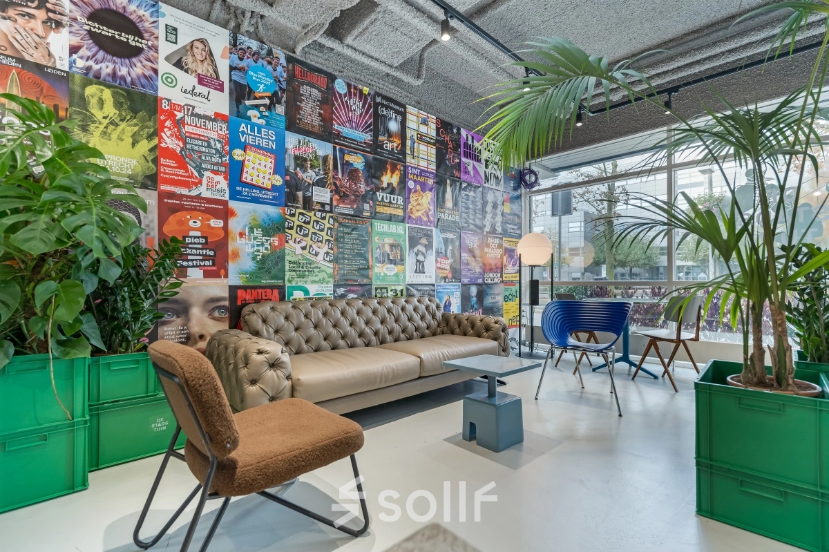 Lively office lounge at Daltonlaan 200, Utrecht Rijnsweerd, featuring colorful posters, a comfortable sofa, stylish chairs, and lush greenery, ideal for informal meetings. A unique twist for office space rental.