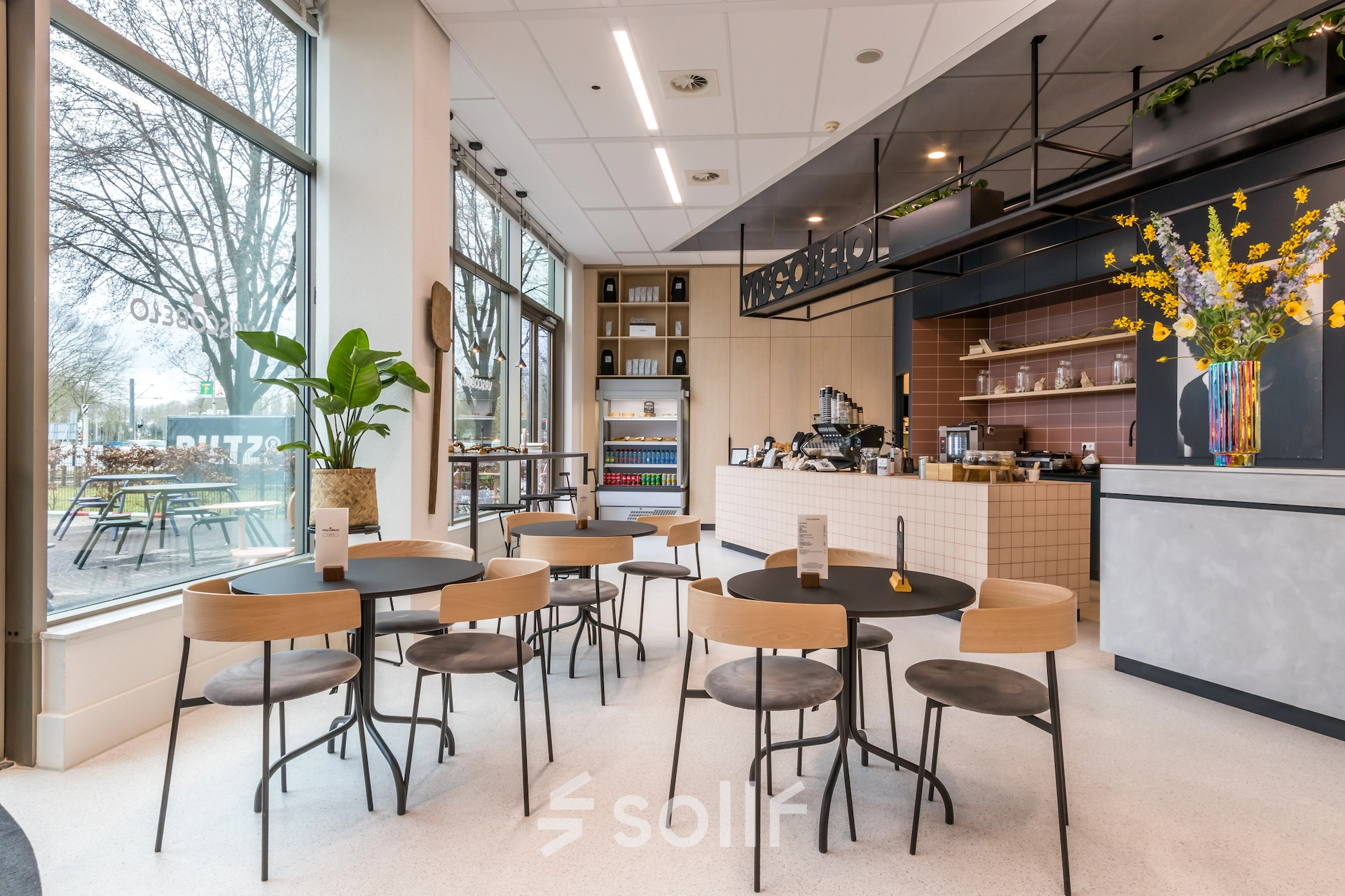 Furnished office space with modern decor and seating in Utrecht South, featuring a counter and several chairs and tables near large windows.