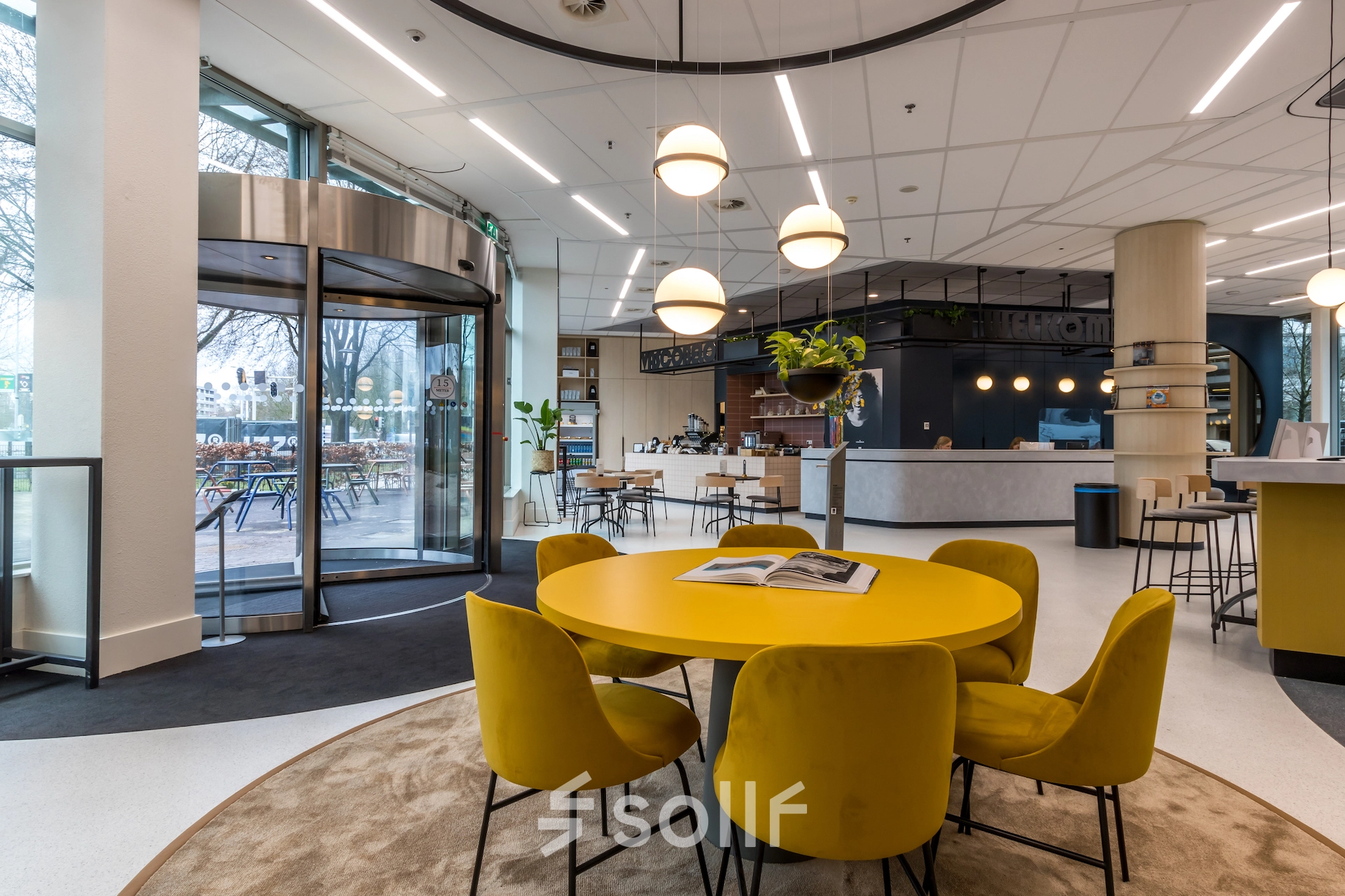 Modern office with round yellow table and chairs, attractive lighting, and reception area in the background, perfect for rent office space in Utrecht South.
