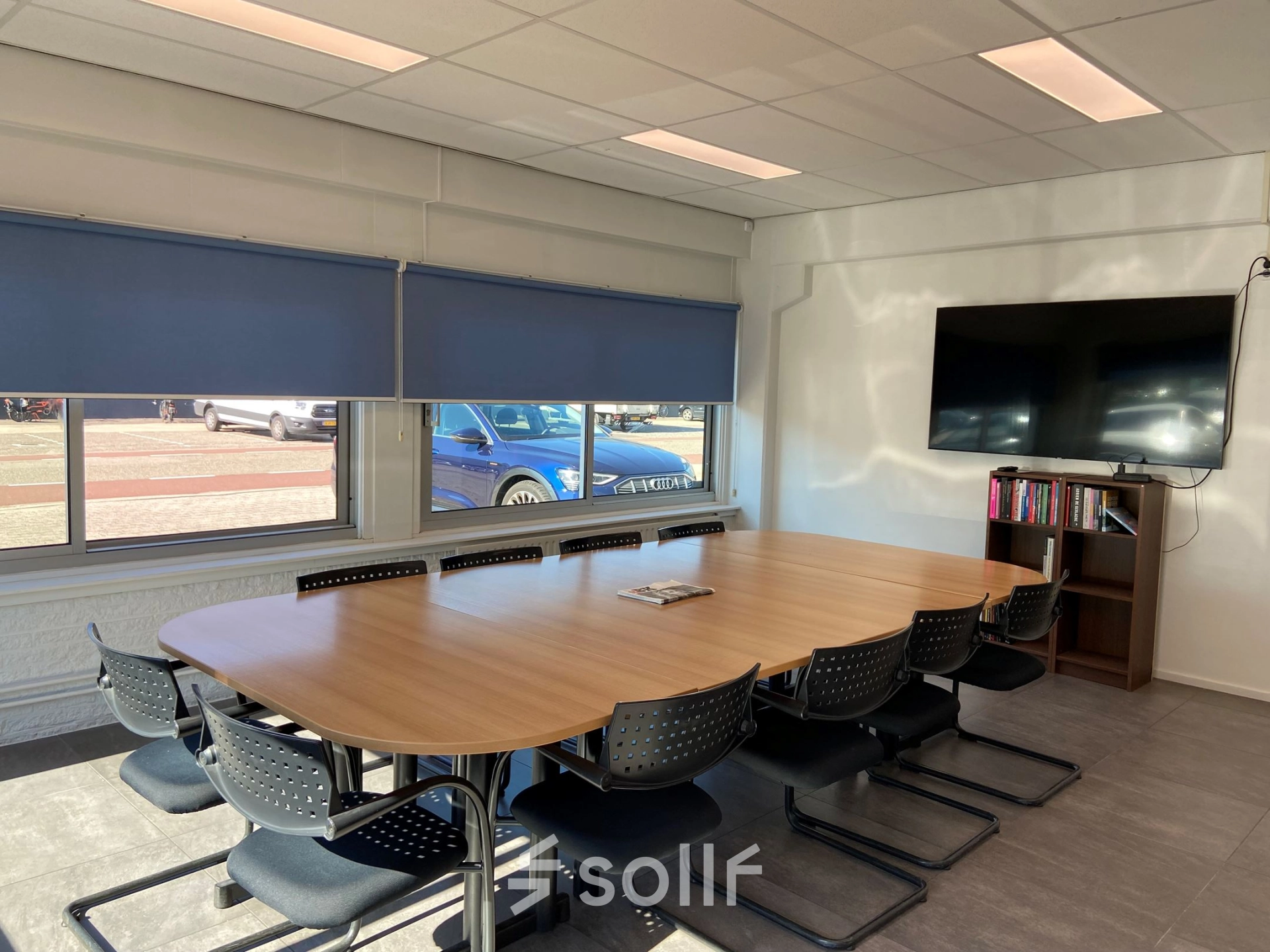 Bright office space for rent at Zonnebaan 54 in Utrecht West, featuring a large conference table, wall-mounted TV, and bookshelf. Ideal for office space rental and meetings.