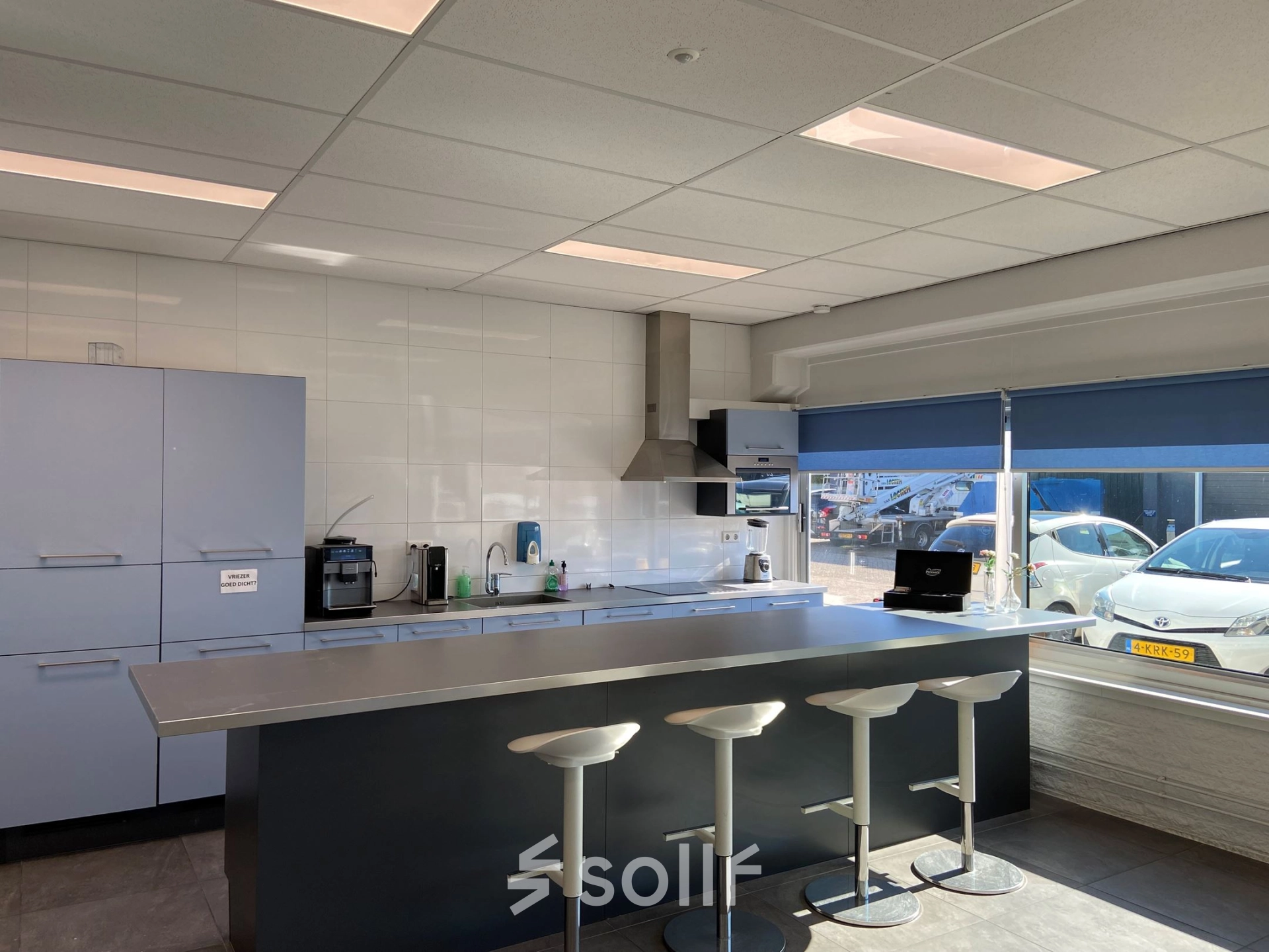 Bright office pantry with bar stools and a window view, suitable for office space rental in Utrecht West.
