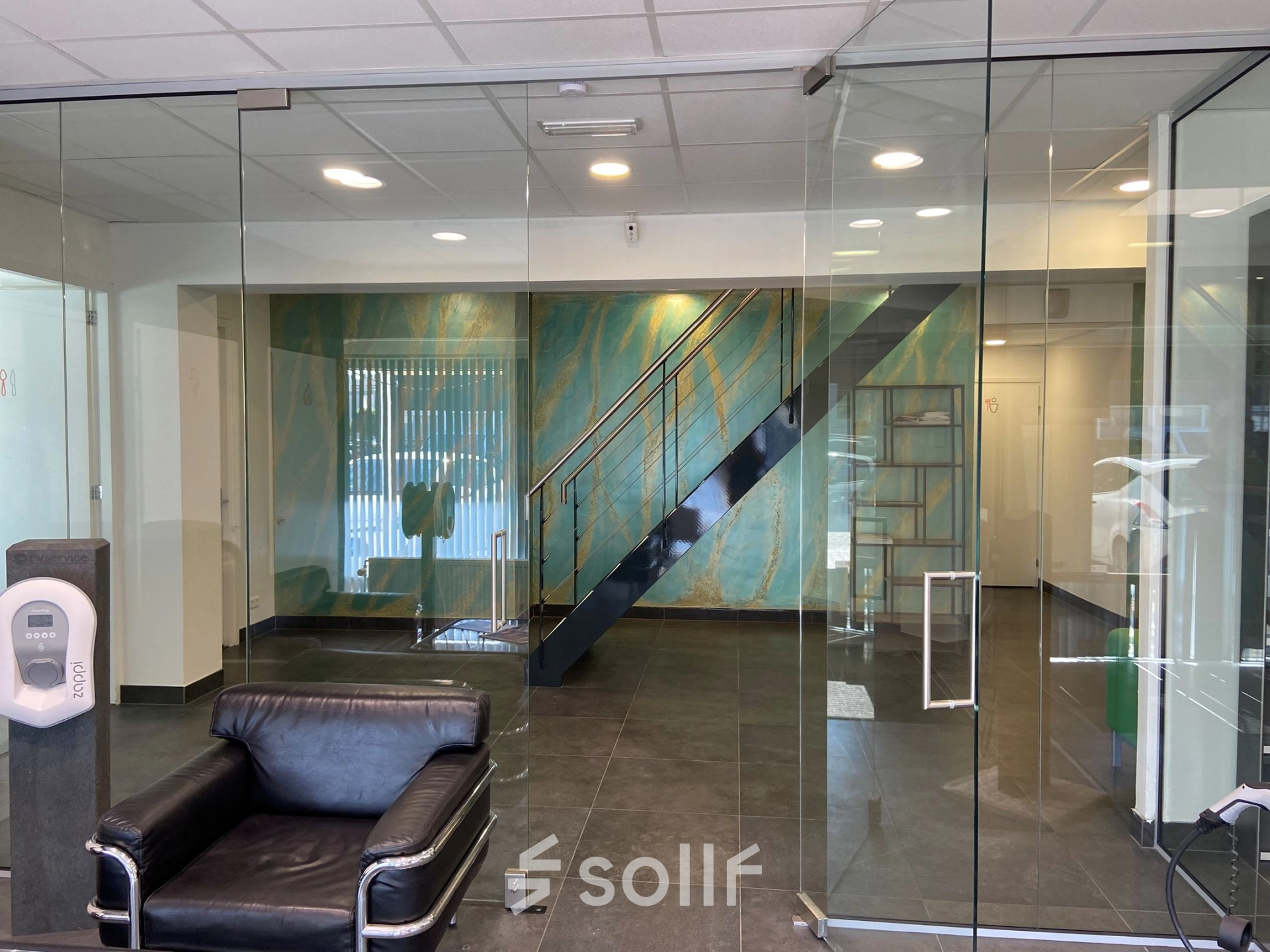 Modern office entrance with glass walls and a black leather chair at Zonnebaan 54, ideal for those seeking office space rental in Utrecht West.