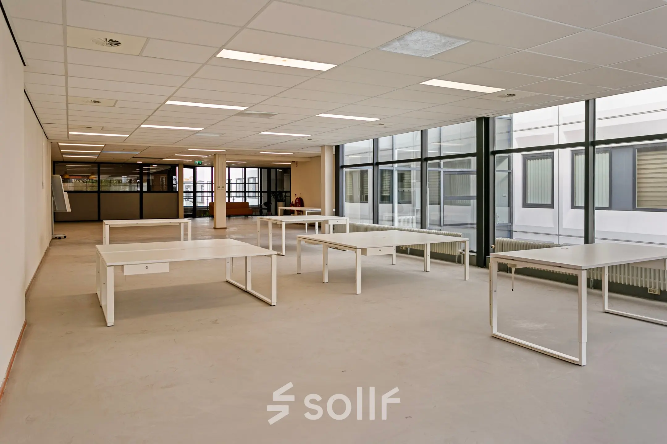 Spacious office space with large windows and several desks at De Run 4312, Veldhoven, ideal for businesses seeking office space rental. Neutral tones and ample natural light create a productive work environment.