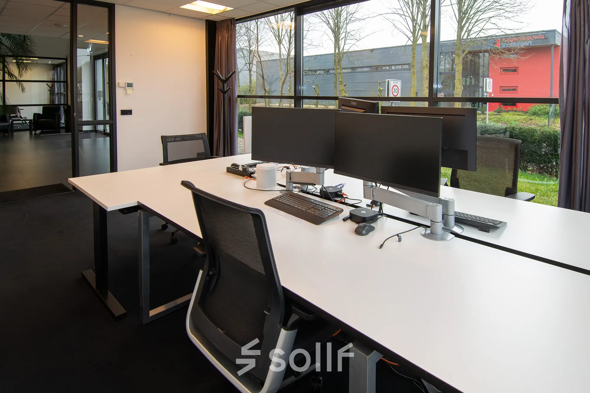 Modern office space at Gildestraat 13, Velp, featuring a sleek workspace with multiple monitors and large windows overlooking greenery, available for office space rental.
