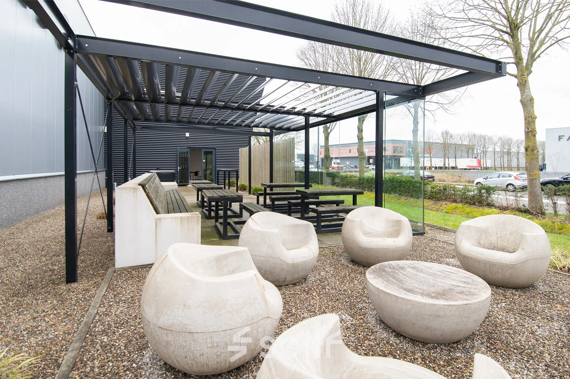 Outdoor seating area at Gildestraat 13 in Velp, ideal for office space rental with a mix of modern benches and sculptural chairs beneath a sleek pergola.