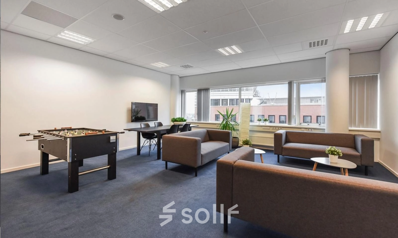 Modern furnished office space for rent at Regulusweg 11, Voorburg, featuring a foosball table, seating area, and large windows.