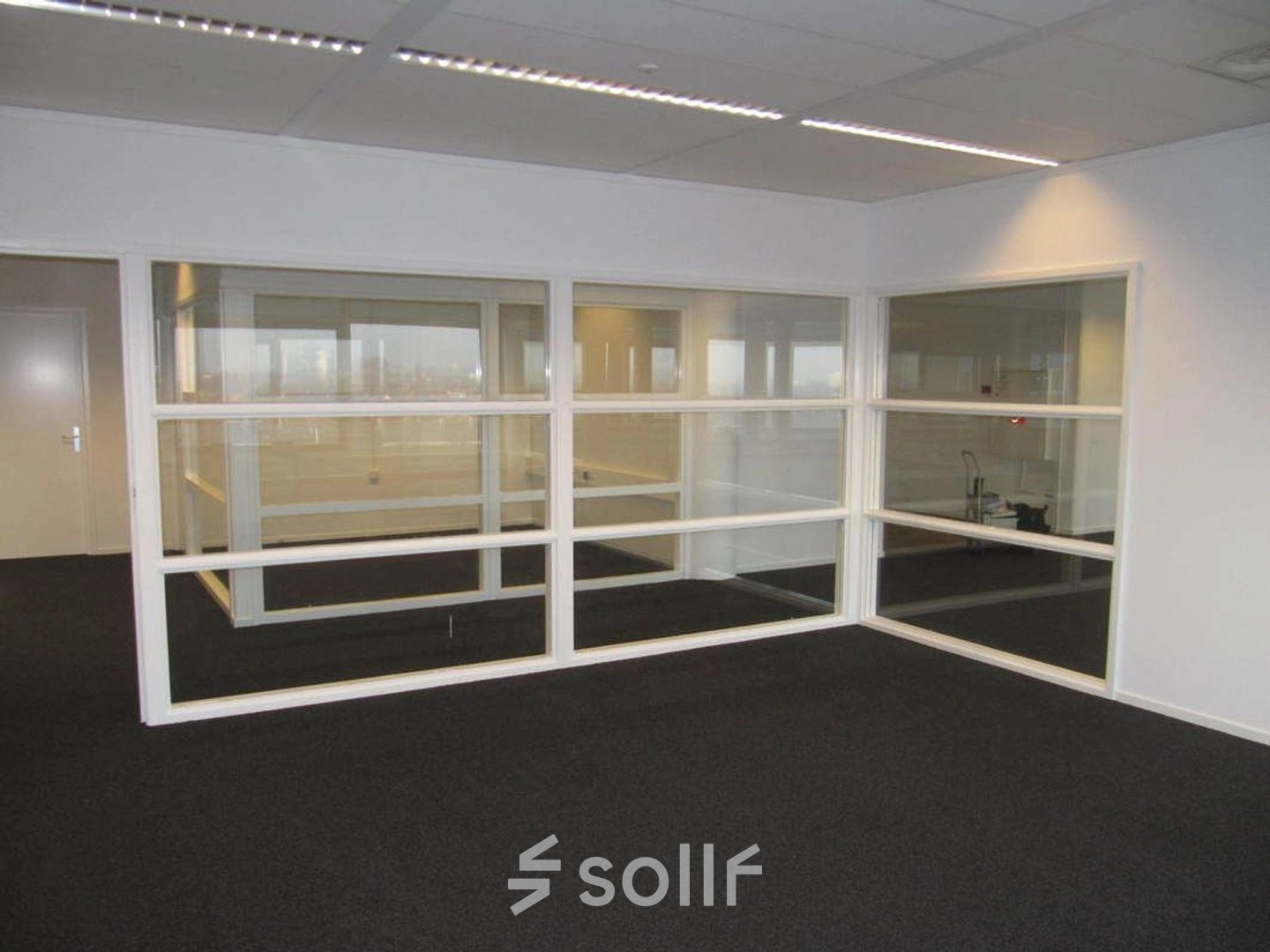 Interior view of office space at Regulusweg 11, Voorburg, featuring glass partitions and carpeted floors, ideal for those looking for office space rental.