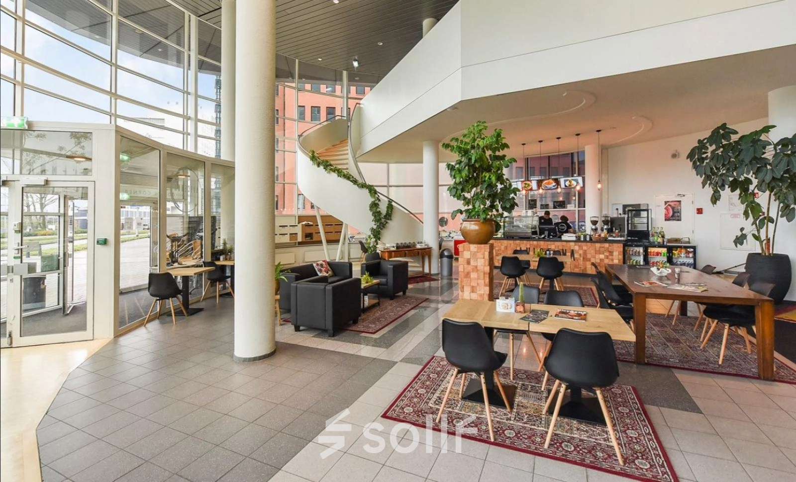 Spacious office lounge at Regulusweg 11, Voorburg featuring modern furniture for rent office space with a relaxed seating area and coffee bar. Numerous plants enhance the inviting atmosphere.