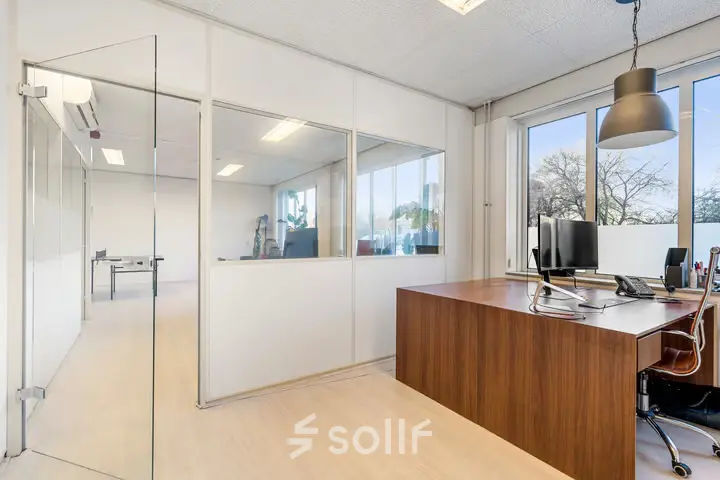 Spacious office to rent at Agro Business Park 22, Wageningen, featuring large windows, a wooden desk, and a computer setup. Ideal for office space rental with an abundance of natural light.