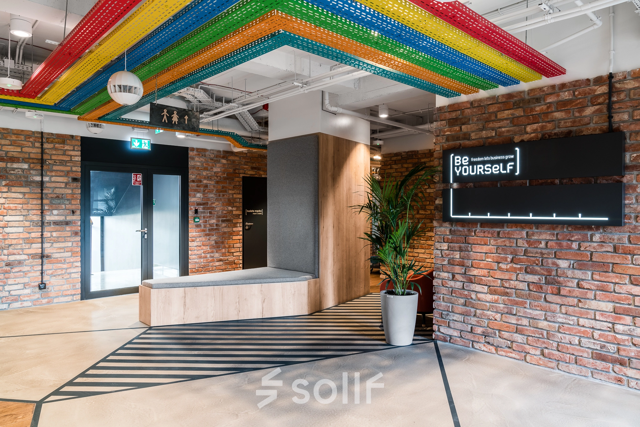 Stylish office space at Konstruktorska 11, Warsaw Mokotow, featuring exposed brick walls and colorful ceiling accents, available for rent.