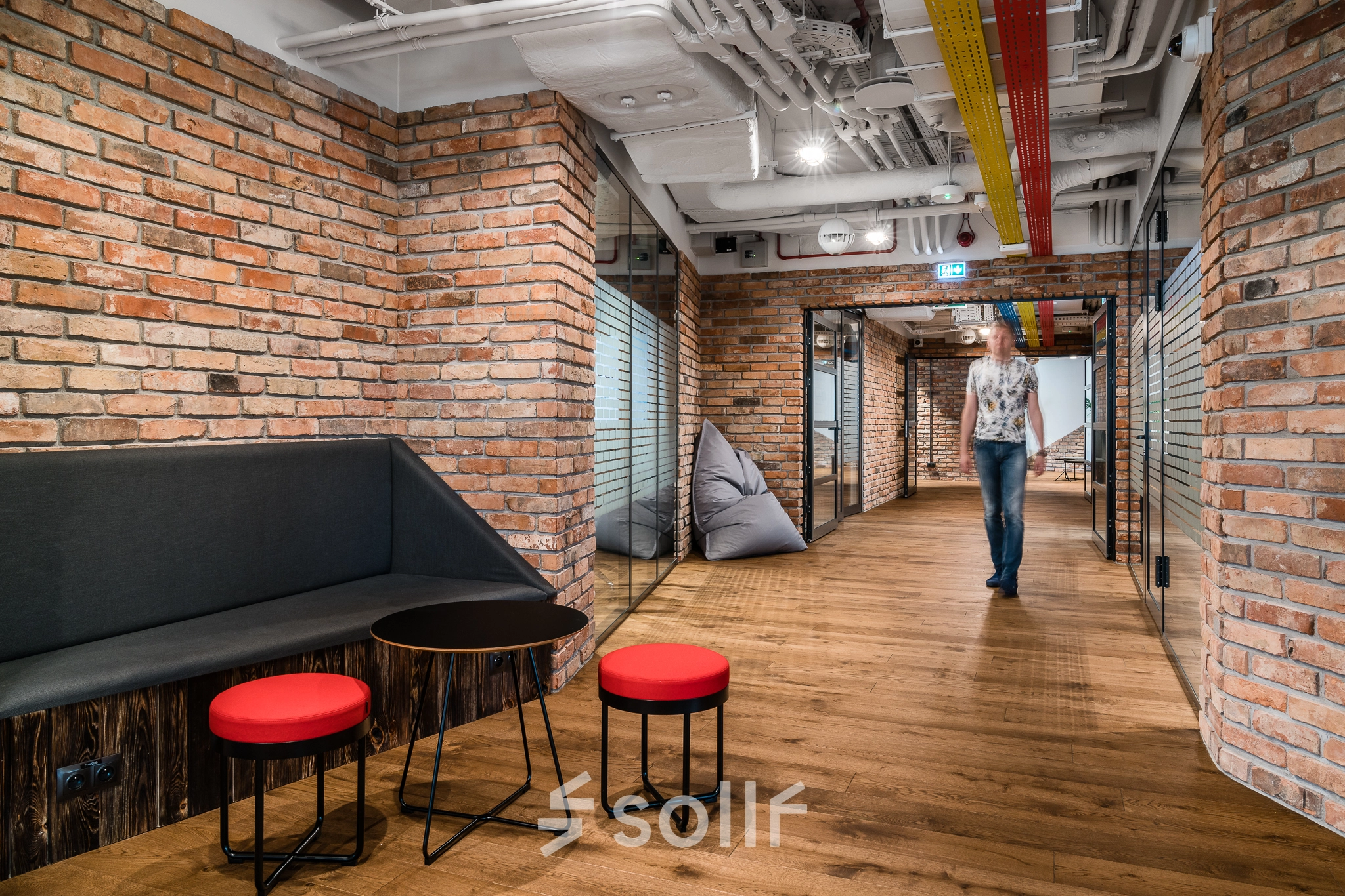 Modern office interior at Konstruktorska 11, Warsaw Mokotow, featuring brick walls, seating area, and a person walking, ideal for office space rental.