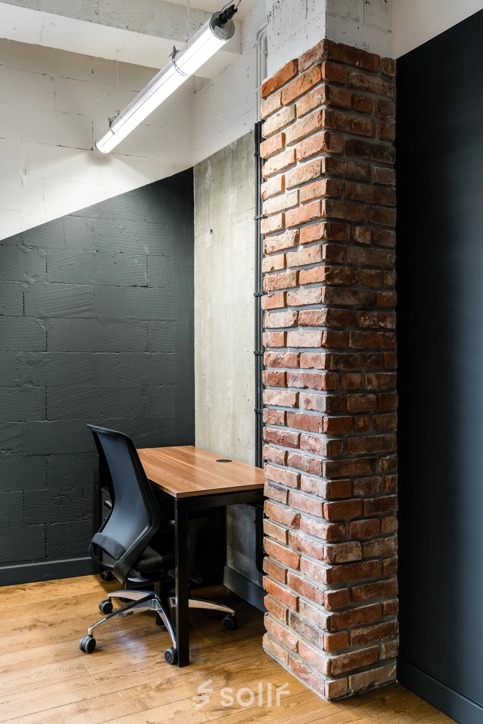 A cozy office space with a brick column, wooden flooring, and a desk with an office chair, ideal for office space rental in Warsaw Mokotow.